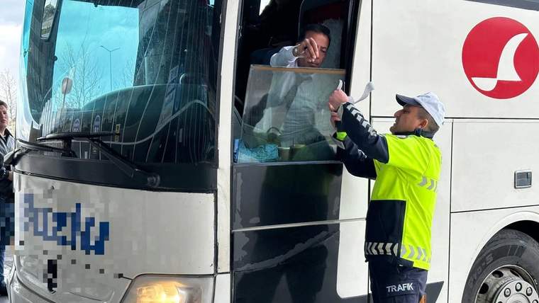 Trafik görevlisi, beyaz bir otobüsün açık kapısındaki sürücüye elindeki belgeyi uzatıyor.
