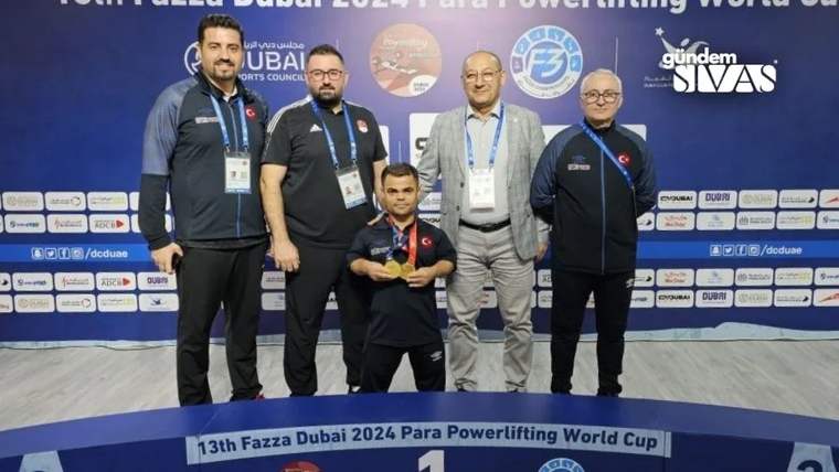 Dört kişi, bir altın madalya tutan kısa boylu bir sporcunun etrafında duruyor.