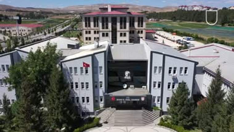 Ağaçlarla çevrili, önünde merdivenler bulunan çok katlı bir kamu binasının havadan görünümü.