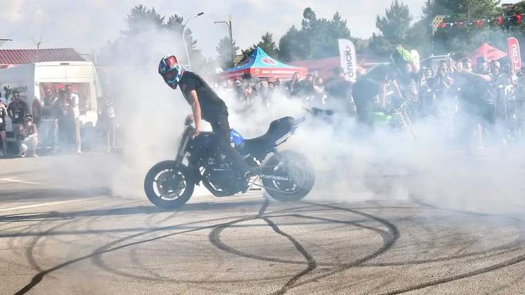 Motosiklet tutkunlarının buluşmasında, bir motosiklet sürücüsü duman içinde kaydırma yapıyor.