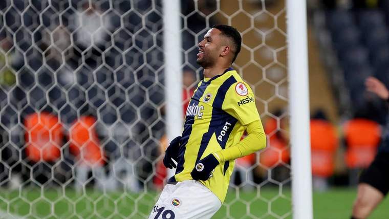 Sarı-lacivertli forması ve beyaz şortuyla bir futbolcu, kale ağlarının önünde sevinçle duruyor.