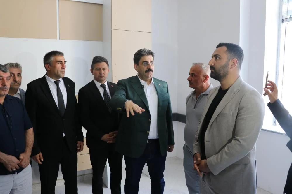 Aydınlık bir iç mekânda duran bir grup erkekten biri elini uzatırken diğerleri onu dinliyor.
