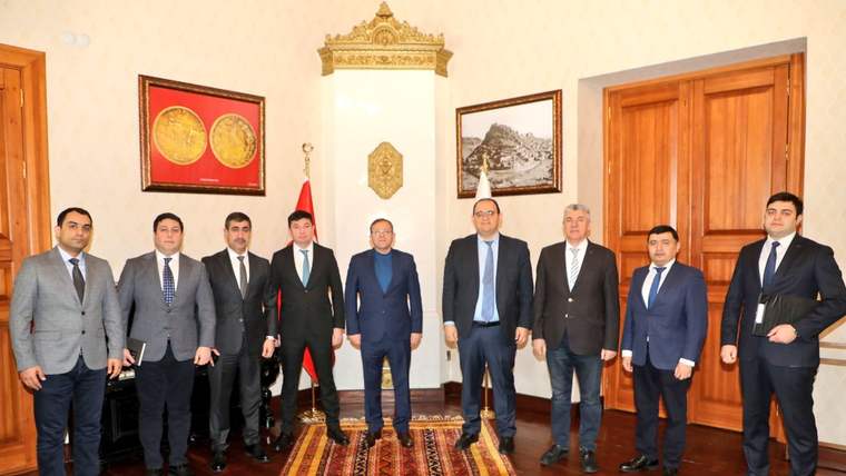 Süslü bir odada takım elbiseli dokuz erkek, duvarlardaki tabloların önünde yan yana duruyor.