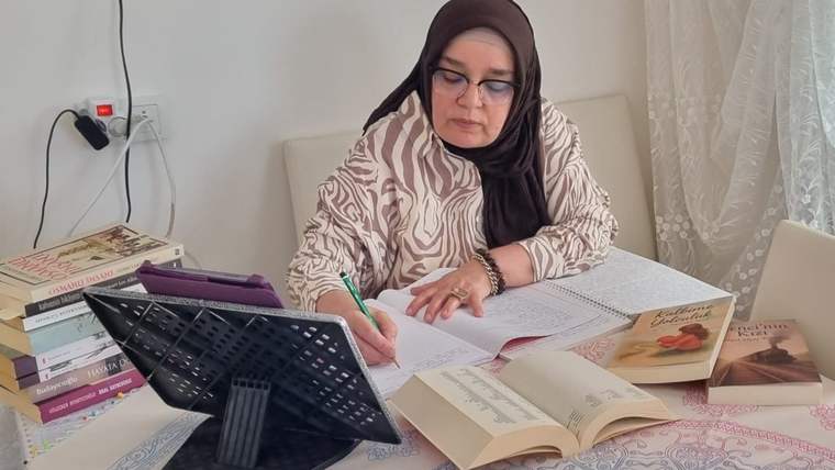 Bir kadın, masada not alırken etrafında kitaplar var.