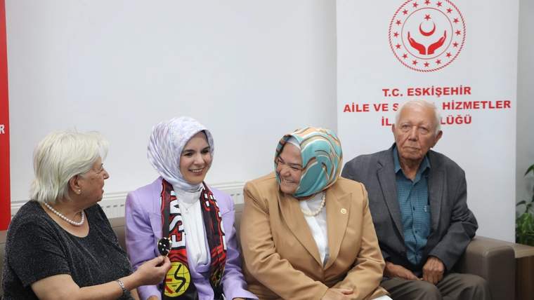 Dört kişi koltukta otururken başörtülü bir kadın, yanındaki yaşlı kadınla sohbet ediyor.