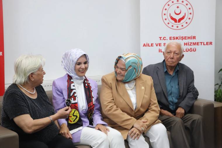 Dört kişi koltukta otururken başörtülü bir kadın, yanındaki yaşlı kadınla sohbet ediyor.
