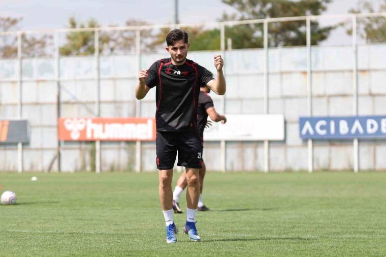 Siyah forması ve şortuyla bir futbolcu, antrenman sahasında top sürerken ellerini kaldırıyor.