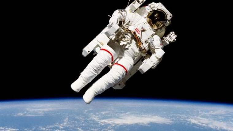 Uzayda, astronot kıyafeti giymiş bir kişi, Dünya'nın mavi yüzeyinin üzerinde süzülüyor.