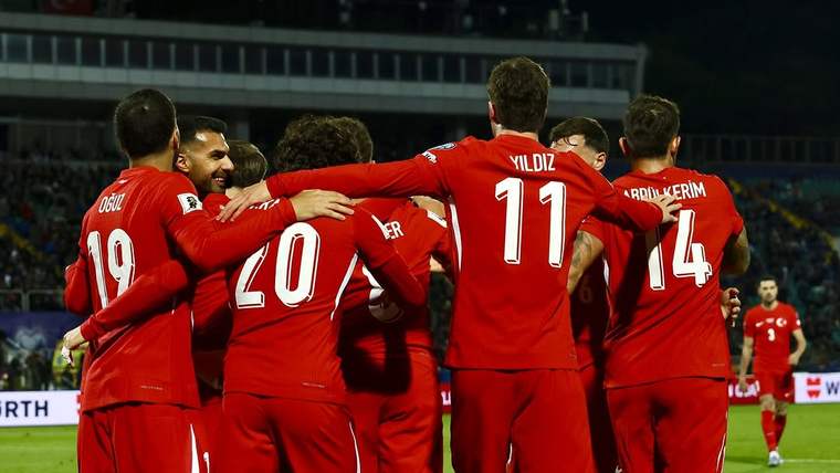 Kırmızı formalı futbolcular, saha içinde birbirlerine sarılarak kutlama yapıyor; arkada tribünler görülüyor.
