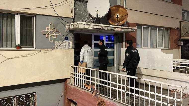 Apartman girişinde iki polis memuru ve beyaz önlük giyen bir kişi, korkulukların arkasında duruyor.