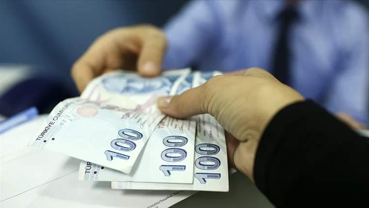 Bir el, diğerine 100 TL banknotları veriyor. Arka planda bir masa ve kişi silueti görünüyor.