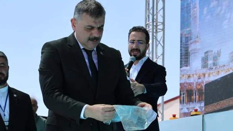 Temel atma töreninde bir kişi, elinde mavi bir örtü tutuyor.