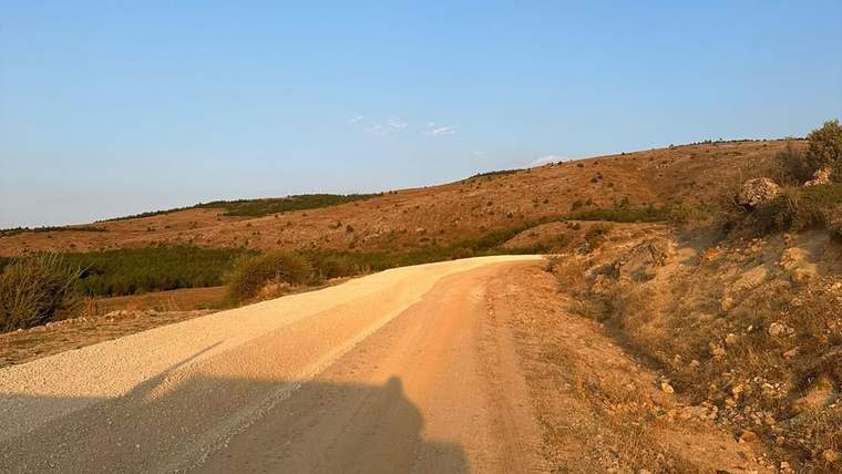 Kırmataş serilmiş toprak yol, kuru tepeler ve seyrek ağaçların arasından kıvrılarak uzanıyor.