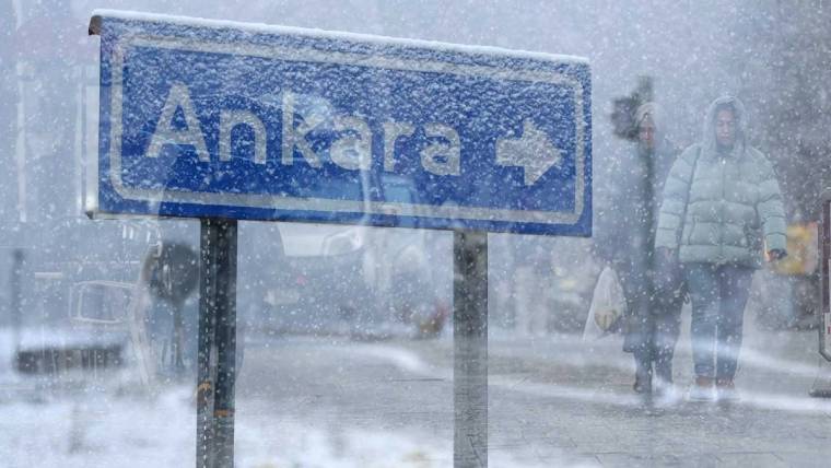 Yoğun kar yağışı altında, üzerinde Ankara yazan mavi yön tabelası ve kaldırımda yürüyen kişiler görülüyor.