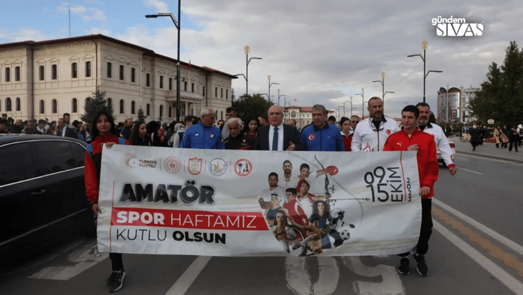 Bir grup kişi, üzerinde “Amatör Spor Haftamız Kutlu Olsun” yazılı pankartı cadde üzerinde taşıyor.