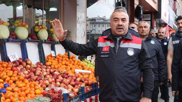 Zabıta ekipleri, meyve tezgahının önünde durarak denetim yapıyor.
