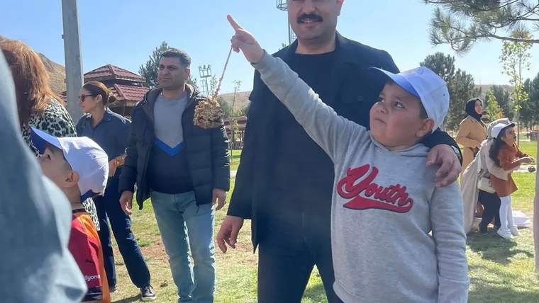 Parkta bir çocuk gökyüzünü işaret ederken yanında duran bir adam ve çevredeki insanlar görülüyor.
