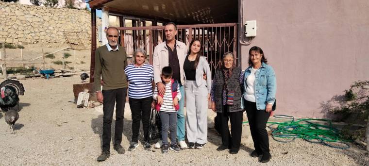 Bir evin önünde, aralarında çocukların da bulunduğu yedi kişi ve bir köpek birlikte duruyor.