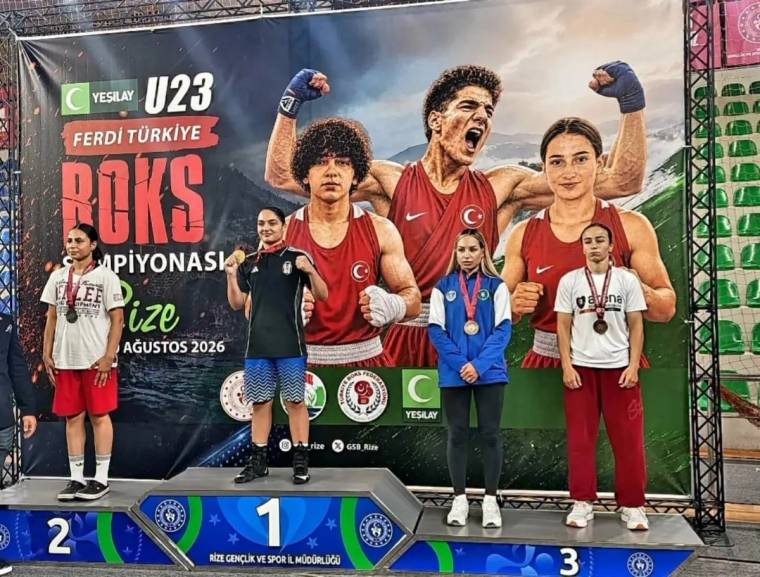 Boks turnuvası pankartı önünde sporcular, üç basamaklı podyumda poz veriyor; ortada iki boksör bulunuyor.