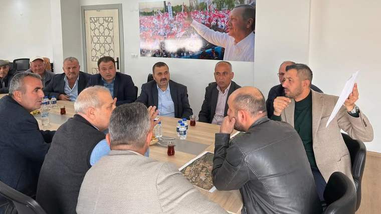 Masanın etrafında oturan bir grup erkek, iç mekânda çay bardakları ve harita eşliğinde konuşuyor.