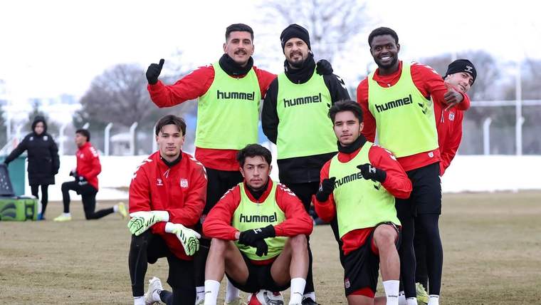 Antrenman yapan futbolcular, yeşil yelek giymiş ve gülümseyerek poz veriyor.