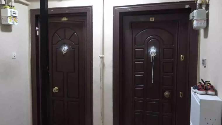 Apartman koridorunda yan yana iki koyu renkli kapı, üstlerinde gaz sayaçları ve sağda ayakkabılık görülüyor.