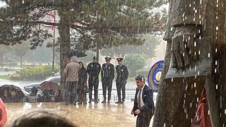 Şiddetli yağmur altında üniformalı dört kişi ve takım elbiseli bir kişi ıslak zeminde duruyor.