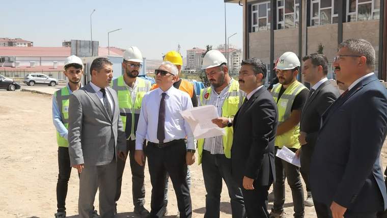 İnşaat alanında, inşaat ekipmanlarıyla birlikte çalışan kişiler ve yöneticiler belgeleri inceliyor.