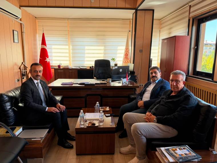 Ofis odasında bir masa çevresinde oturan üç erkek ve arkalarında Türk bayrağı görülüyor.