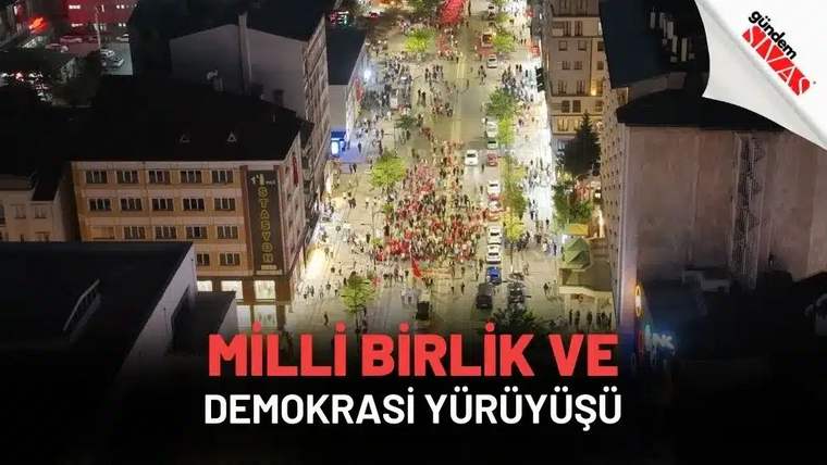 Kalabalık bir grup, sokakta yürüyüş yapıyor, etrafta Türk bayrakları var.
