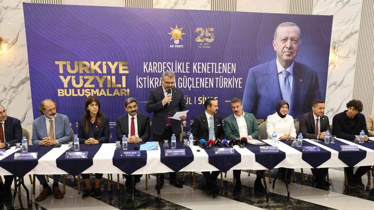 Mor ve sarı pankart önünde, masada oturan kişilerin bulunduğu toplantıda bir kişi ayakta konuşuyor.