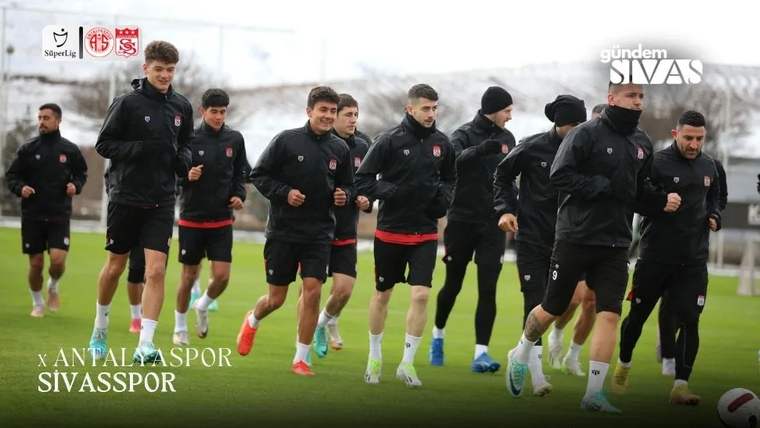 Siyah antrenman kıyafetleri giyen futbolcular, yeşil sahada birlikte koşu yapıyor; görselde takım adları yazıyor.