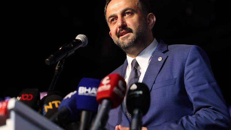 Kürsüde duran takım elbiseli bir kişi, önündeki çok sayıda mikrofonla konuşma yapıyor.