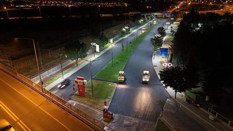 Gece aydınlatılan bölünmüş yolda birkaç araç ilerlerken çevrede ağaçlar ve yol tabelaları görülüyor.