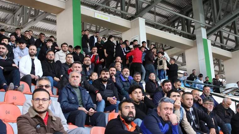Kapalı tribünde turuncu koltuklarda oturan ve ayakta duran çok sayıda seyirci görülüyor.