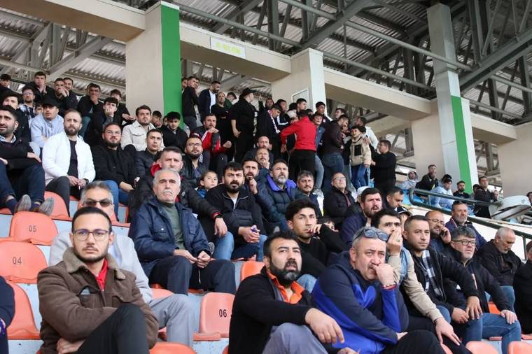 Kapalı tribünde turuncu koltuklarda oturan ve ayakta duran çok sayıda seyirci görülüyor.