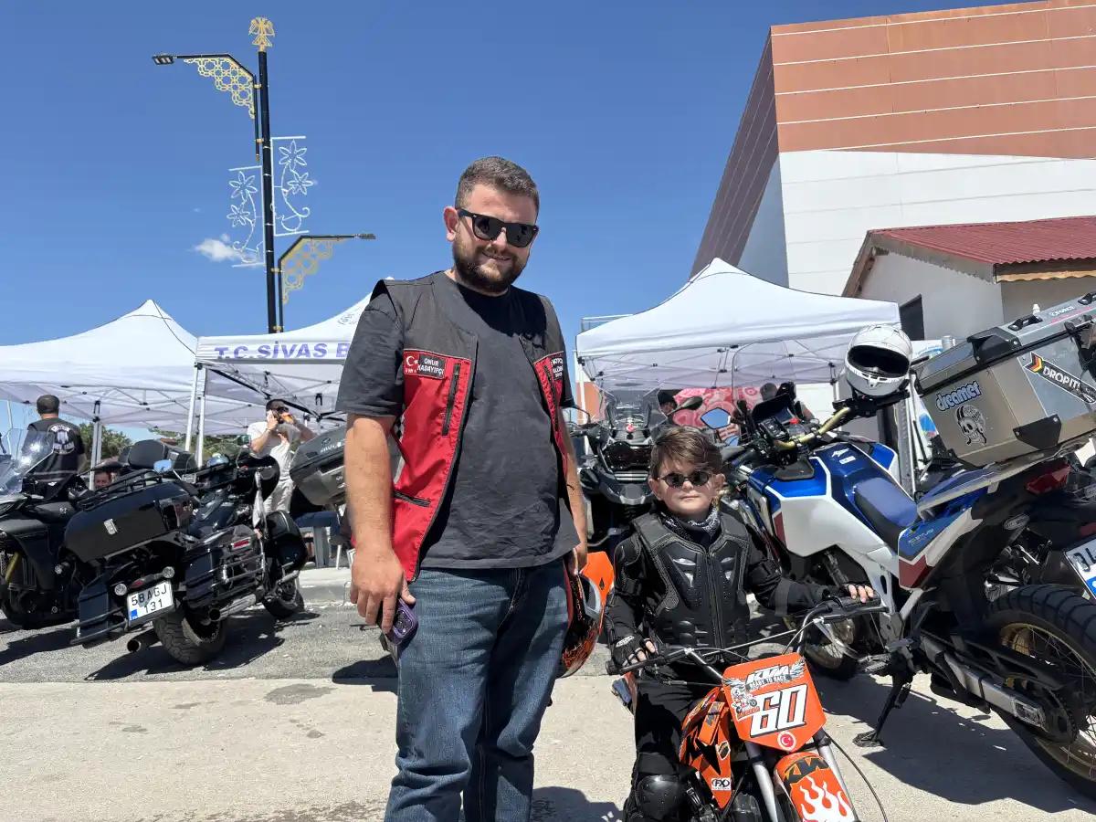 Bir yetişkin ve çocuk, motosikletlerin bulunduğu alanda turuncu bir motosikletin yanında duruyor.