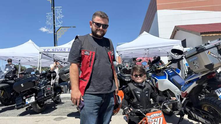 Bir yetişkin ve çocuk, motosikletlerin bulunduğu alanda turuncu bir motosikletin yanında duruyor.