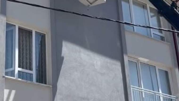 Bir binanın dış cephesinde pencereler, balkon korkulukları, klima ünitesi ve yatay bir kablo görülüyor.