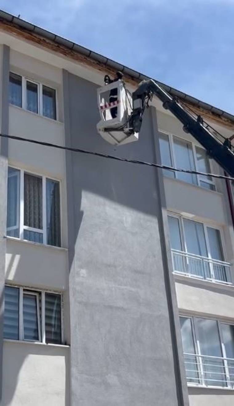 Bir binanın dış cephesinde pencereler, balkon korkulukları, klima ünitesi ve yatay bir kablo görülüyor.