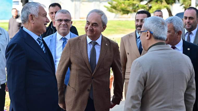 Açık havada, takım elbiseli ve ceketli birkaç kişi ayakta durarak sohbet ediyor.