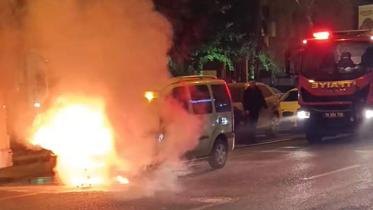 Gece yolda alevler içinde yanan otomobilin yanında itfaiye aracı ve bir kişi görülüyor.