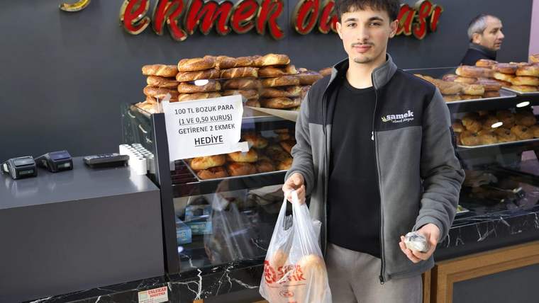 Fırın tezgâhında ekmekler sergilenirken genç bir kişi elinde poşet ve bozuk paralarla duruyor.