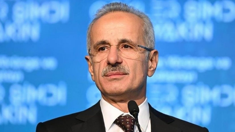 Mikrofonun önünde duran bir kişi, arka planda mavi bir afiş var.