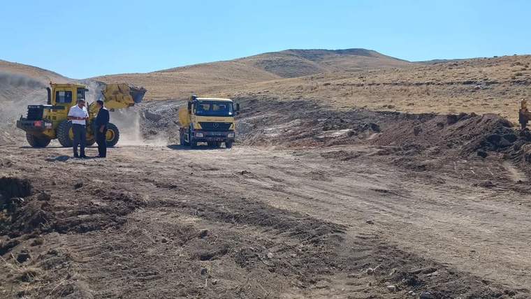 Yol çalışması yapılan alanda bir kamyon ve iş makinesi, işçiler etrafta duruyor.