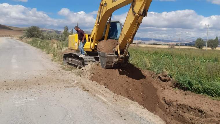 Bir iş makinesi, yol kenarında toprak kazma çalışması yapıyor.
