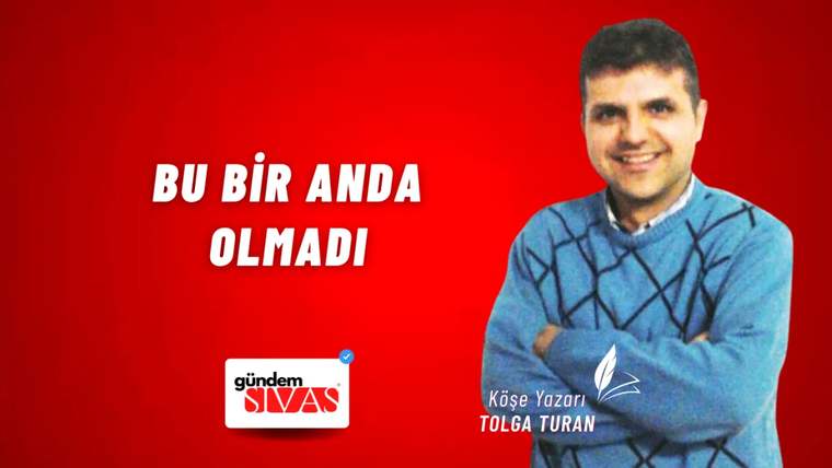 Kırmızı arka planda, mavi kazak giymiş bir kişi gülümsüyor ve kollarını kavuşturmuş.