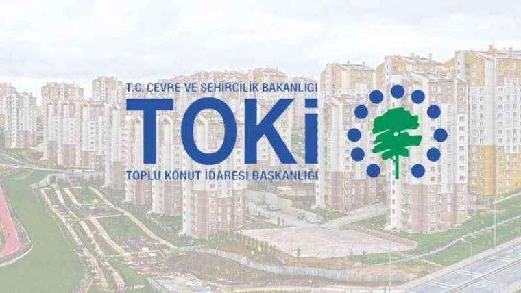 TOKİ logosu, arka planda çok katlı konut binalarının ve düzenlenmiş bir yerleşim alanının üzerinde yer alıyor.