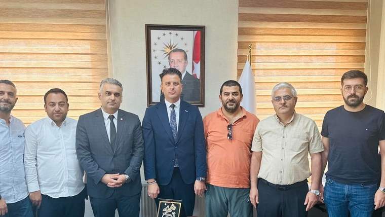 Bir grup erkek, bir ofiste yan yana duruyor; masada belgeler ve bir ödül var.