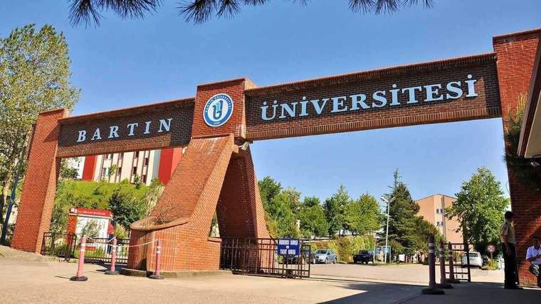 Üzerinde Bartın Üniversitesi yazan tuğla giriş takı, çevresindeki ağaçlar ve kampüs yolu görülüyor.